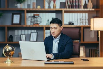 Fototapeta premium Concentrated businessman working on laptop in classic office, looking at monitor screen