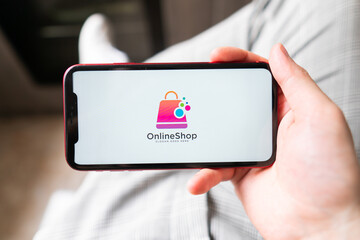 Smart phone online shopping in young man's hand. Desk with coffee in the background. Buy clothing accessories shoes from e-commerce website
