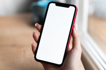 Young woman hands holding mobile smart phone with mockup white blank display, empty screen at home. Shopping, delivery apps, social media applications ads,  close up view.