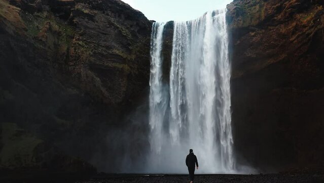 Man walking to Icelandic waterfall Skogafoss in Iceland, near the Skogar, slow-motion background wallpapers. Beautiful landscape. High quality 4k footage. Wide angle shot