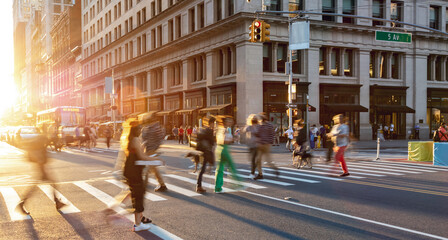 Sunlight shining on people in motion walking across a busy street intersection in Manhattan New York City - 497503375