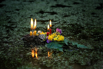 flowers, pentagram amulet, burning candles on dark water, covered aquatic plants duckweeds. old...