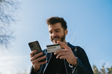 Close up of man hands holding credit card and mobile phone, shopping online. Happy young man freelancer receive payment focus on his face.