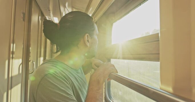 Young attractive tourist, looker out of the window of a moving train at sunset