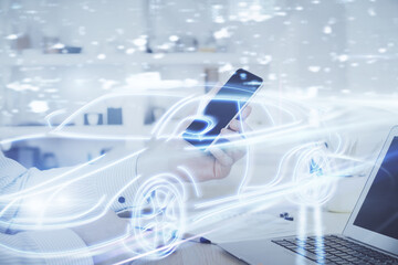Double exposure of man's hands holding and using a digital device and automobile theme hologram drawing. Technology concept.