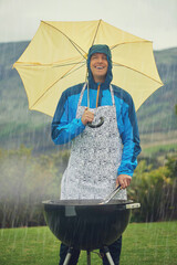 Its like liquid sunshine. Shot of a man happily barbecuing in the rain.