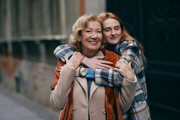 Grandmother and adolescent granddaughter enjoy the autumn walk on the street. They are smiling and hugging.