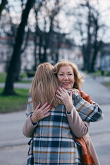 A grandmother is hugging her adult granddaughter in the park. They are greeting, and happy to see each other.