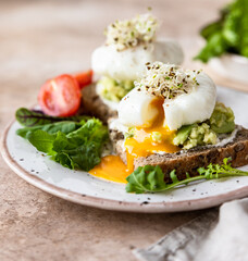 Sourdough bread with cream cheese, mashed avocado and poached egg served with salad leaves, tomatoes and sprouts. Healthy breakfast or brunch. Diet food concept.