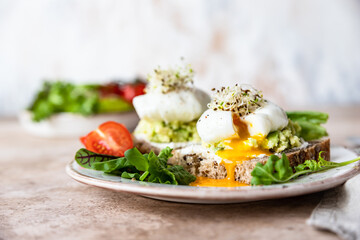 Sourdough bread with cream cheese, mashed avocado and poached egg served with salad leaves, tomatoes and sprouts. Healthy breakfast or brunch. Diet food concept.