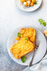 French brioche toast with physalis, honey and mint on ceramic plate, grey background. Traditional sweet breakfast with fried bread with egg and milk. Top view.