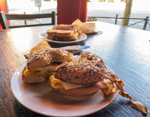 Breakfast sandwiches at a cafe - An everything bagel with bacon and egg in the foreground.