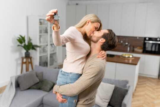 Woman holding home keys while kissing with her boyfriend in new apartment. Lovely couple feeling ecstatic about their recent purchase of new home which makes them feel being on the verge of happiness