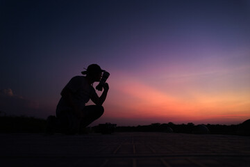 Photographer's silhouette with the gear on hand and in his knees in the golder hour