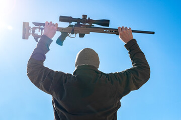 Capitulating soldier sniper rifles with an optical sight in man`s hands give up winter day blue sky