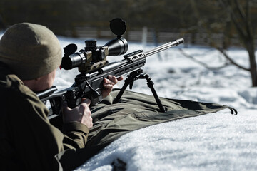 A sniper rifles with an optical sight in man`s hands aimimg back view winter day