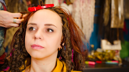 Unrecognizable person makes hairstyle for young woman in salon. Professional hairstylist makes hairdo for client.