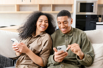 Woman sitting at the couch and looking at the smartphone of her boyfriend. Multiracial couple with...