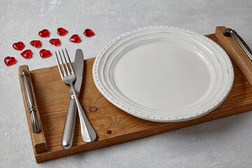 An empty white plate with cutlery on a wooden tray
