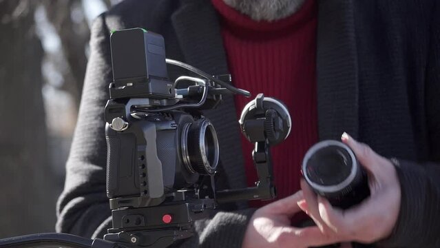 A filmmaker replaces the lens on a digital film camera. Close-up shot.