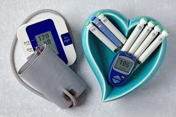 Blood pressure monitor, blood glucose monitor, insulin syringe pens in a blue heart-shaped bowl