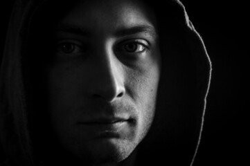 Close up portrait in black and white of a young man with a hood on his head looking grumpy in a...