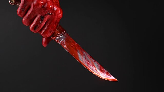 Man holding knife with bloody hand on black background. 