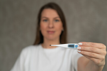 Woman holds an electronic thermometer in her hands, showing 36.6 degrees Celsius