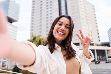 Pretty young female with big smile having fun taking cheerful selfie in the city. Image of happy  woman isolated make picture with camera