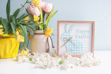 Delicate Easter background of white flowers, petals of colored macaroons and a frame with a bunny and the inscription 