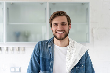 Handsome smiling young man leaning on kitchen counter with vegetables and looking at camera.