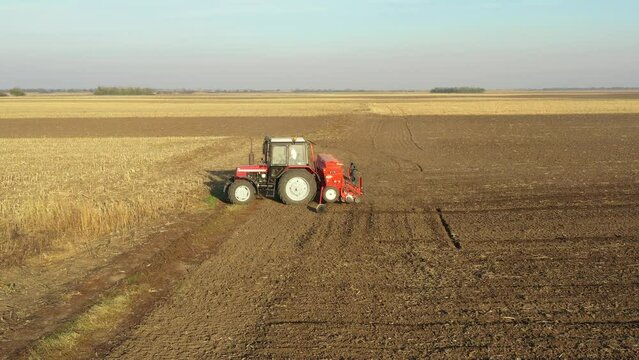Above side shot of tractor as pulling seed drill machine over arable field, soil, planting new wheat crop.