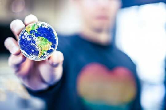 Blurry man, focus on a globe. Hand catching the world to protect and care, future environment in human’s hand concept. Elements of this image furnished by NASA.