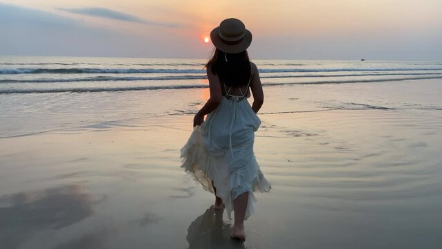 Slow motion woman wearing a white dress walking enjoy on the beach with beautiful sunset on summer vacation in Phuket, Thailand