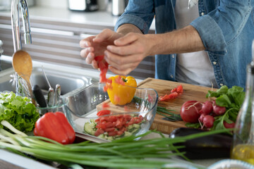 Young man preparing vegetable salad in the kitchen. Happy man making healthy meal