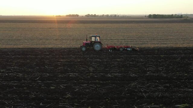 Above dolly move shot of tractor as dragging a disc harrow, harrowing arable field, preparing soil for planting new crop next season.