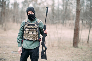 Man stands with pump gun in his hand weared in body armor and balaclava.