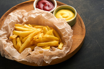 French fries. Tasty French fries server on parchment paper on wooden cutting board with tomato and cheese sauce on wooden table background. Diverse Keto Dishes. Fast food and unhealthy food concept.