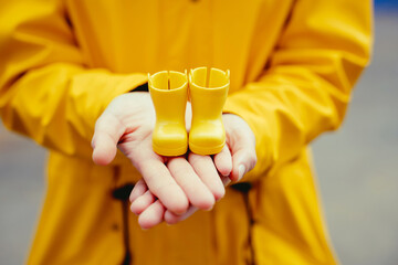 Above shot detail of woman holding a pair of rainy boots in yellow clothes. Horizontal selective focus detail of yellow galoshes isolated in yellow background. Spring conceptual backgrounds.