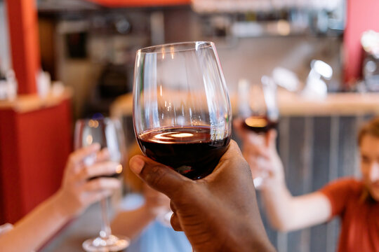people toasting - african american hand holding glass - close up on red wine - raising hands to cheers