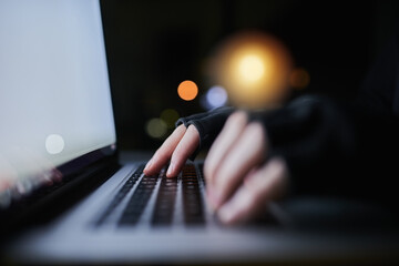 Be careful what you share online. Shot of an unrecognizable computer hacker using a laptop late at...