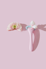 A pink women's razor shaving with white petals and a half ranunculus flower creative flat lay. Beauty hygiene routine. Body positivity movement and gender inclusiveness idea. Pink background.