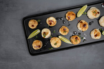 Fried scallops with butter lemon spicy sauce on black plate over old dark stone background.