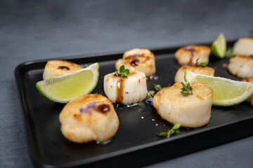 Fried scallops with butter lemon spicy sauce on black plate over old dark stone background.