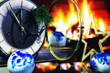 A table clock with an open glass cover surrounded by Christmas decorations against a backdrop of fire.