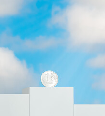 a coin with a denomination of one Russian ruble of silver color stands on a podium in the first place against the background of a blue sky with clouds in the rays of the sun. Russian ruble coins.