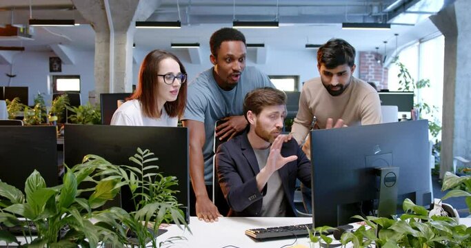 Multiethnic team of males and female cooperating in coworking space. IT team of developers working, laughing and talking in office. Employees of programming company. Brainstorming meeting.