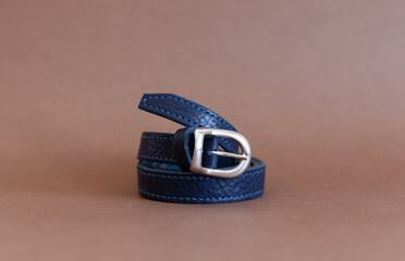 blue woman's belt made of genuine leather, handmade, lie on a brown background.