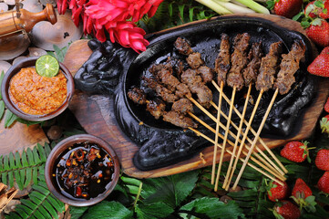 Various dishes - satay, sambal andaliman, salsa macha and red strawberries with artificial leaves