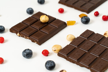 Stack of milk and dark chocolate with nuts, caramel and fruits and berries on a white background.